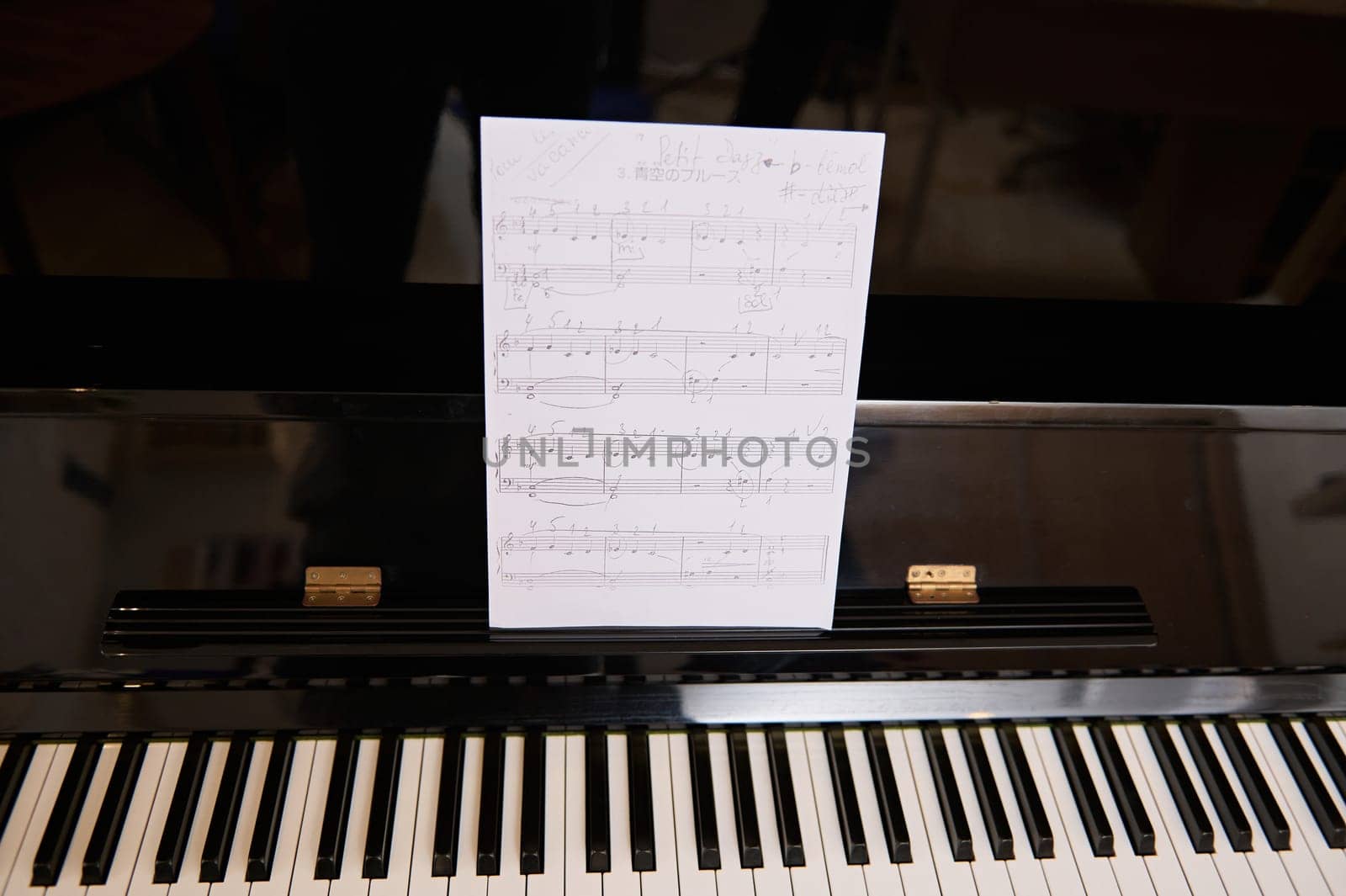 black piano with ebony and ivory keys and white paper sheet with musical notes of classic melody or composition. by artgf