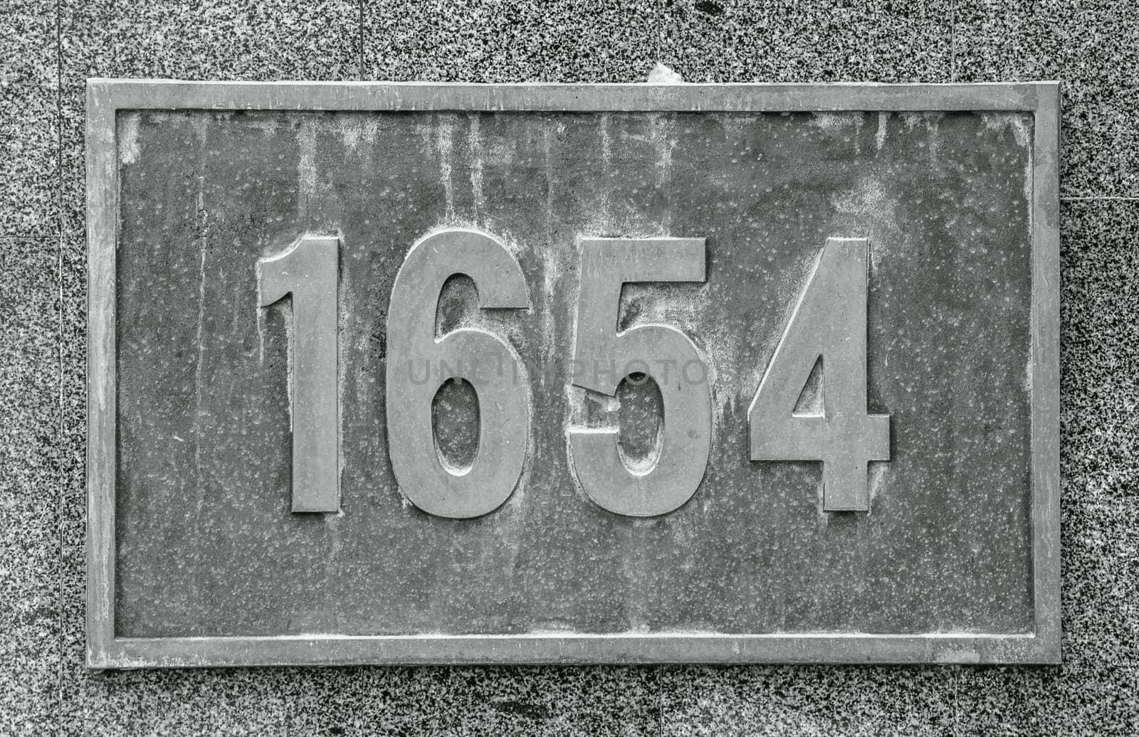 Cast bronze house number on stone wall concept photo. Street exterior metal board plate on wall. A plaque on a brick wall. Street scene, public park. High quality picture.
