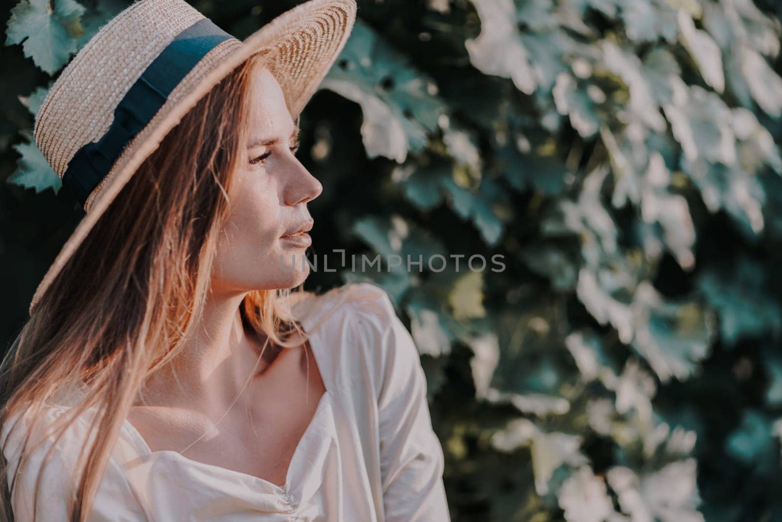 Woman with straw hat stands in front of vineyard. She is wearing a light dress and posing for a photo. Travel concept to different countries.