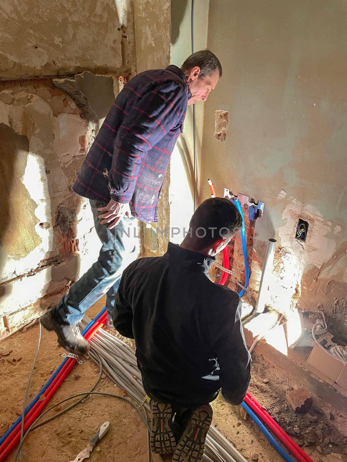 Electrician working working on building site, technicians install wiring by KaterinaDalemans