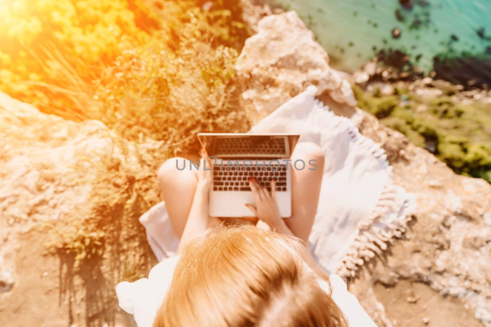 Freelance woman working on a laptop by the sea, typing away on the keyboard while enjoying the beautiful view, highlighting the idea of remote work. by Matiunina