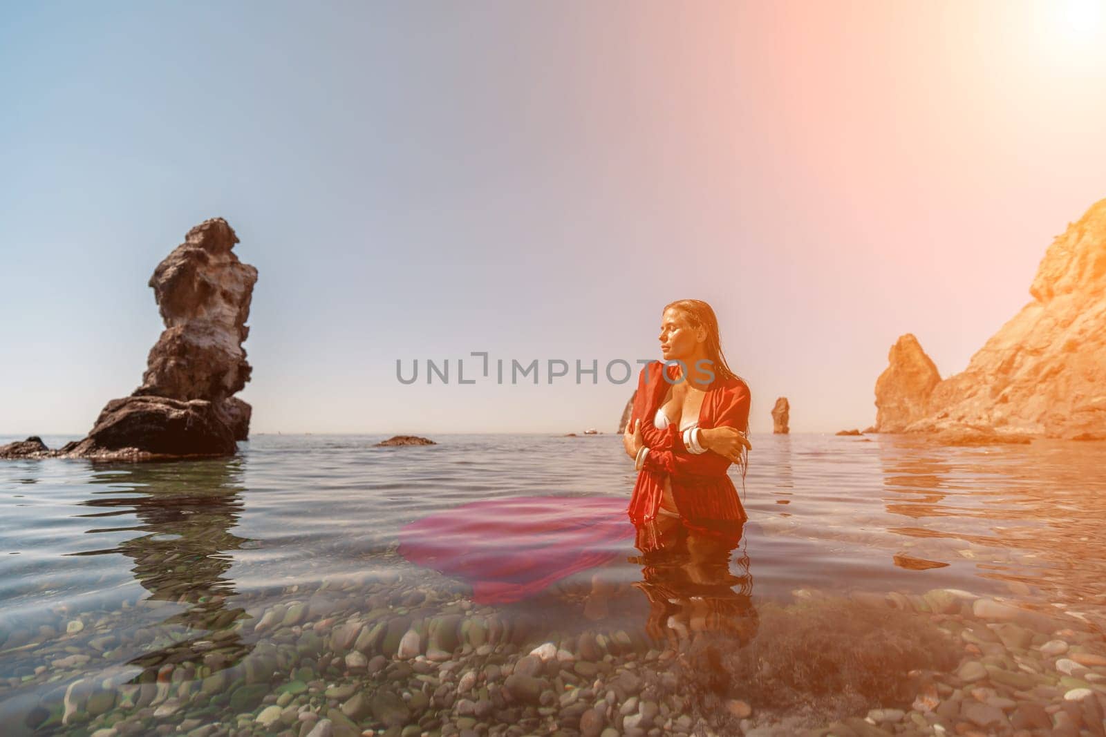 woman sea red dress. Beautiful sensual woman in a flying red dress and long hair, standing in sea in a large bay. by Matiunina