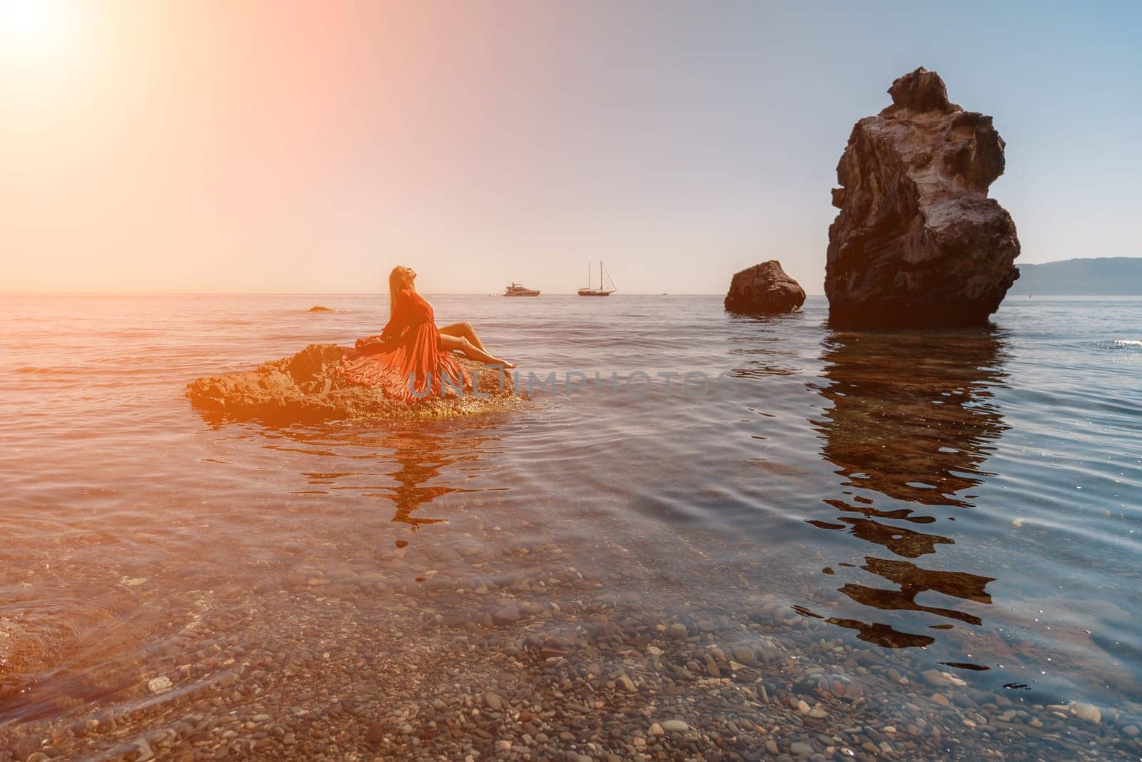 woman sea red dress. Beautiful sensual woman in a flying red dress and long hair, sitting on a rock above the beautiful sea in a large bay