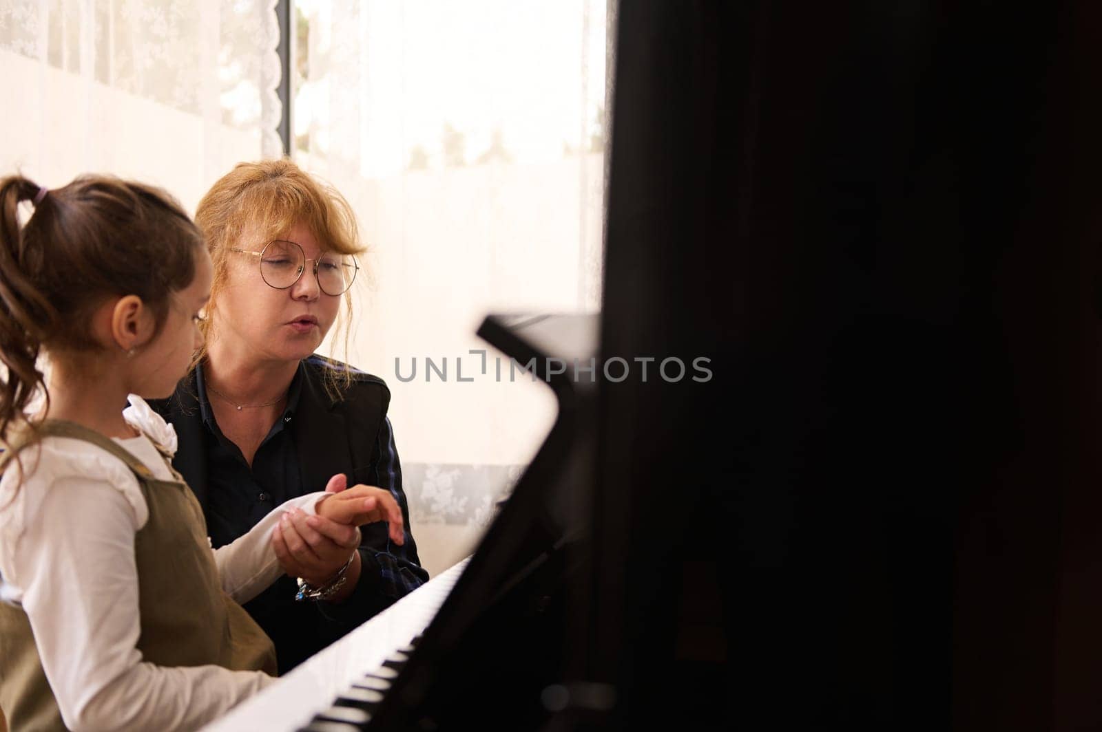 Female pianist teacher holding hands of a student girl, showing her the the truth position of her finger on piano keys by artgf