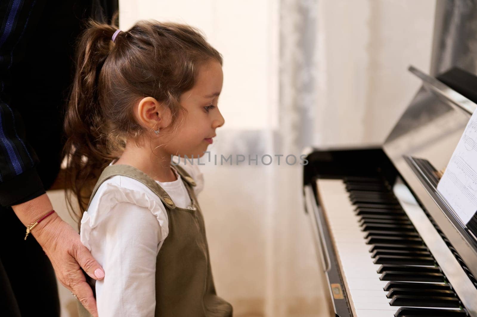 Little girl having individual piano lesson, sitting at pianoforte, ready to learn music with her piano teacher. Authentic portrait of a cute child girl pianist, little talented musician