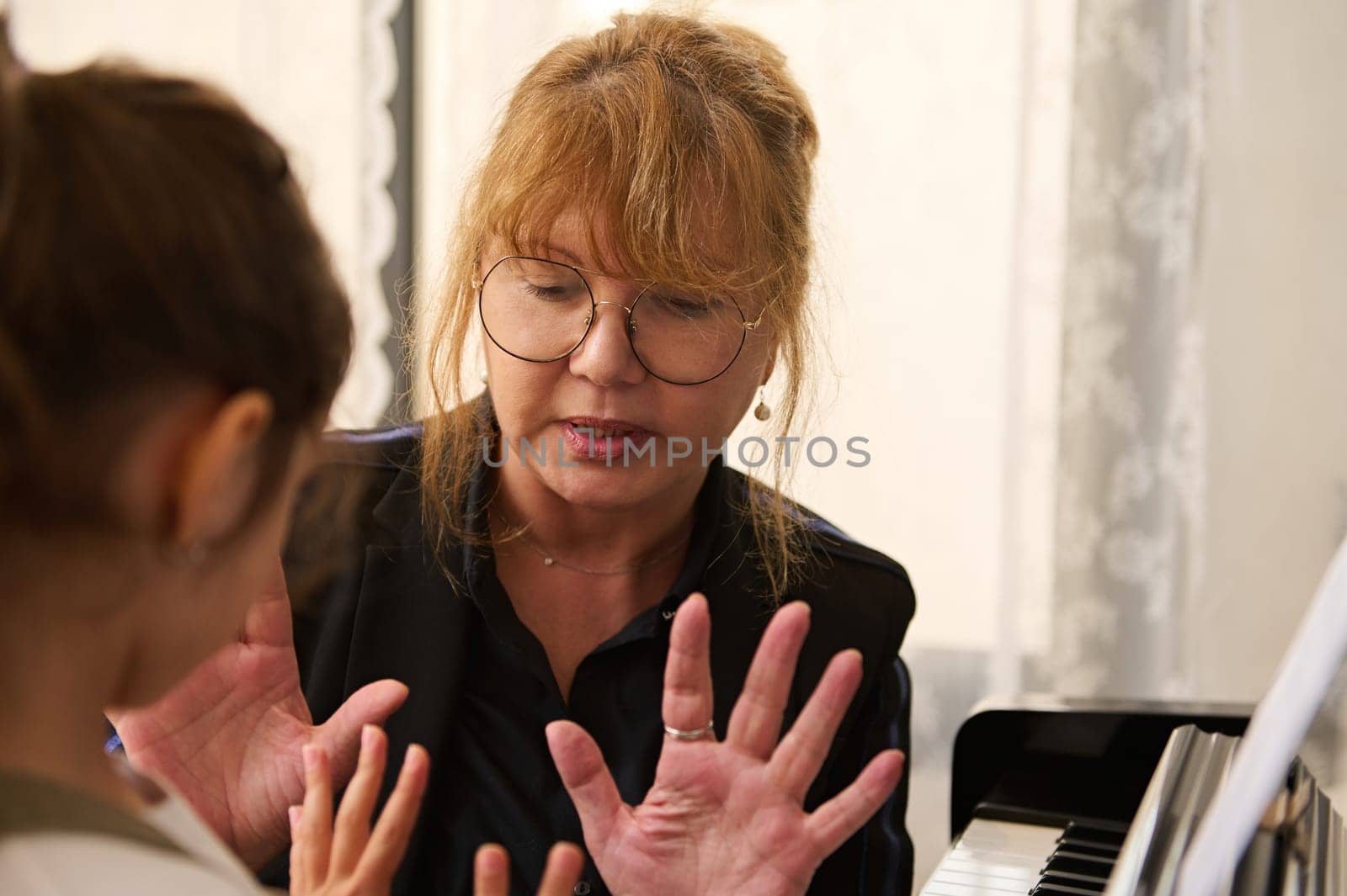 Close-up of Asian mature woman, inspired musician pianist showing to a little student how to play piano during individual music lesson. Kids development and education concept