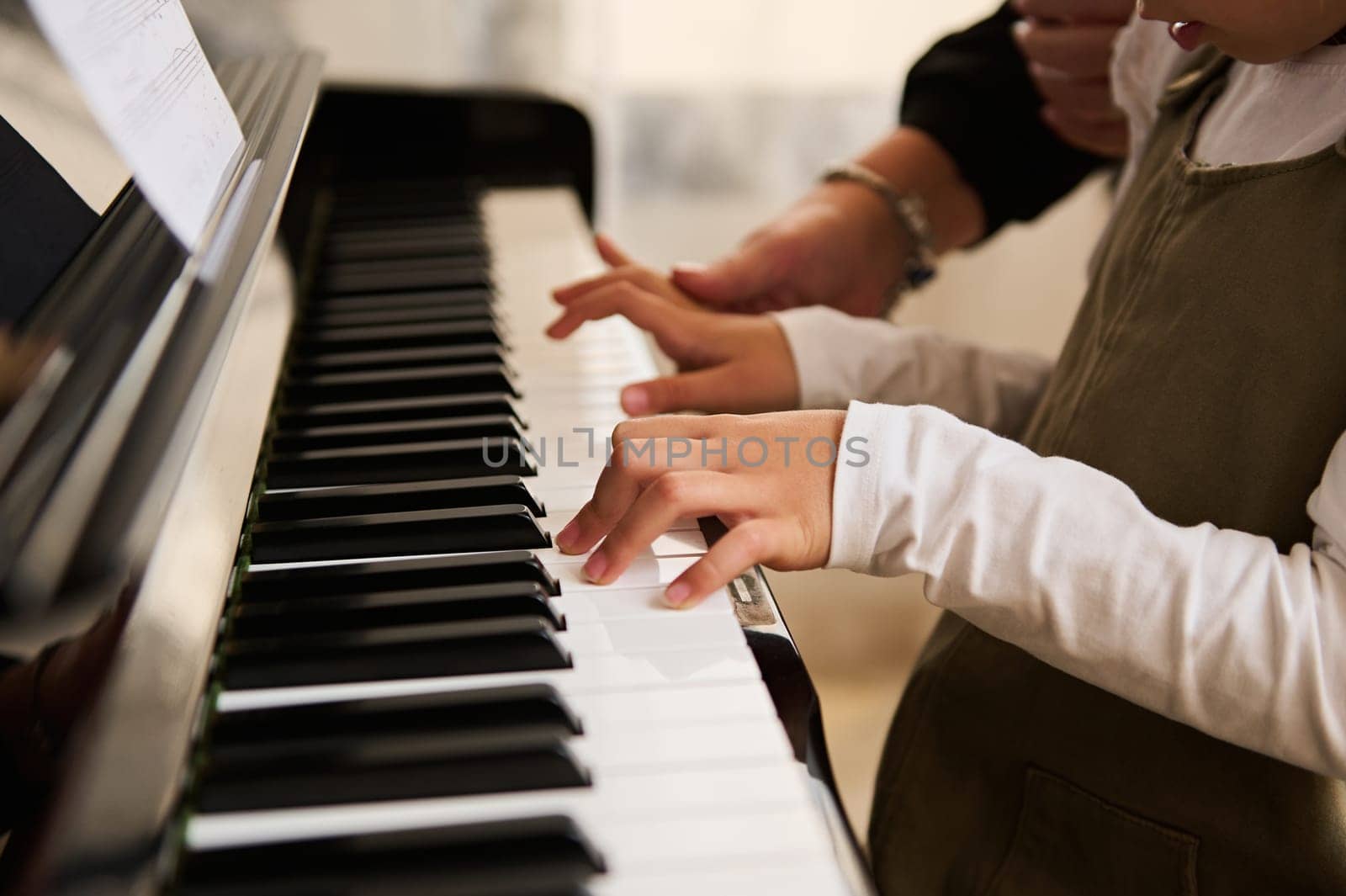 Side view of child's hands on piano keyboard, touching white and black keys while playing music on grand piano. Chord instrument. Music lesson. Arts. Culture. Hobbies and entertainment