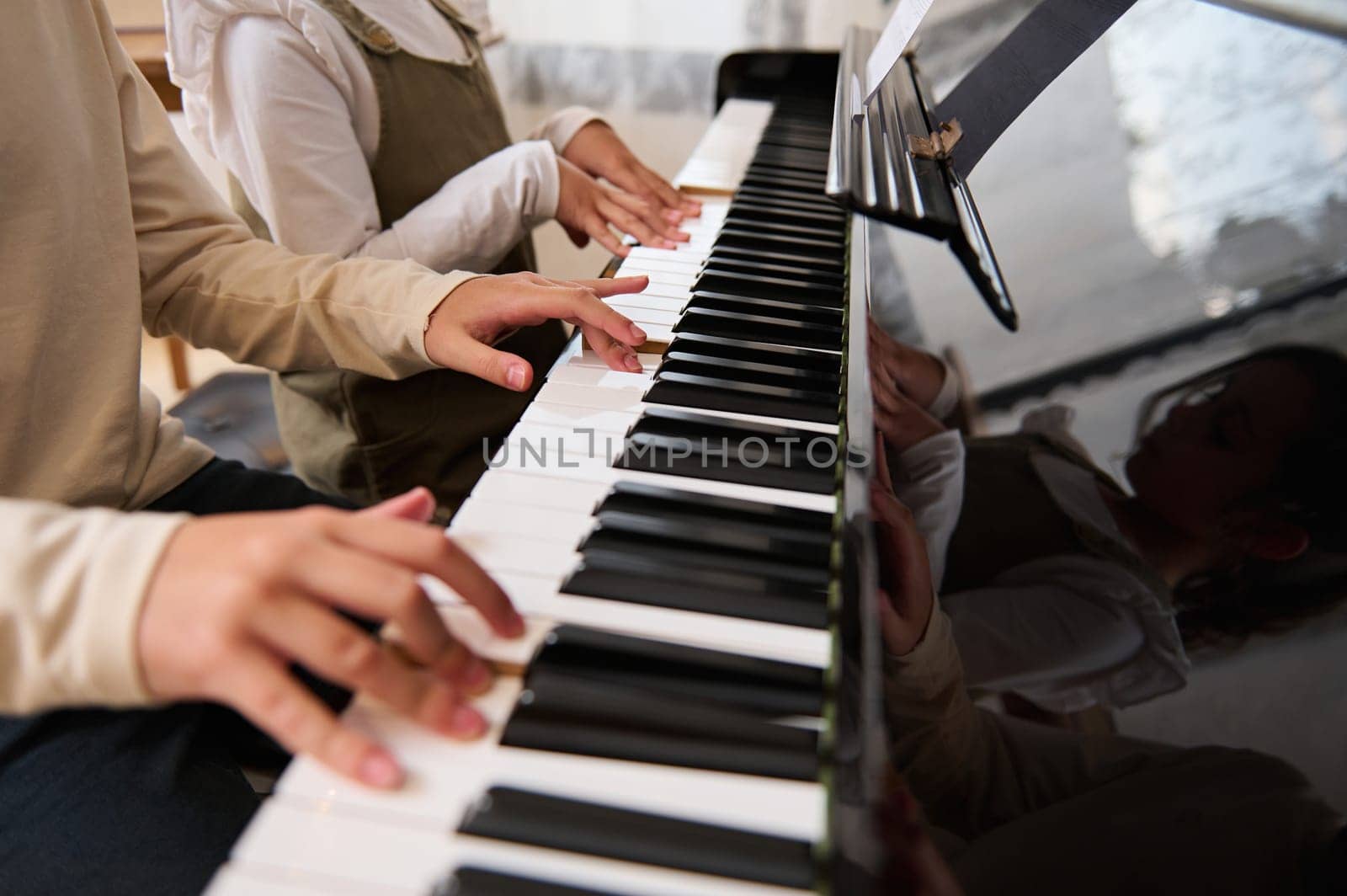 Close-up of the hands of two kids, boy and girl playing music on grand piano. Kids fingers on ebony and ivory keys. Music lesson