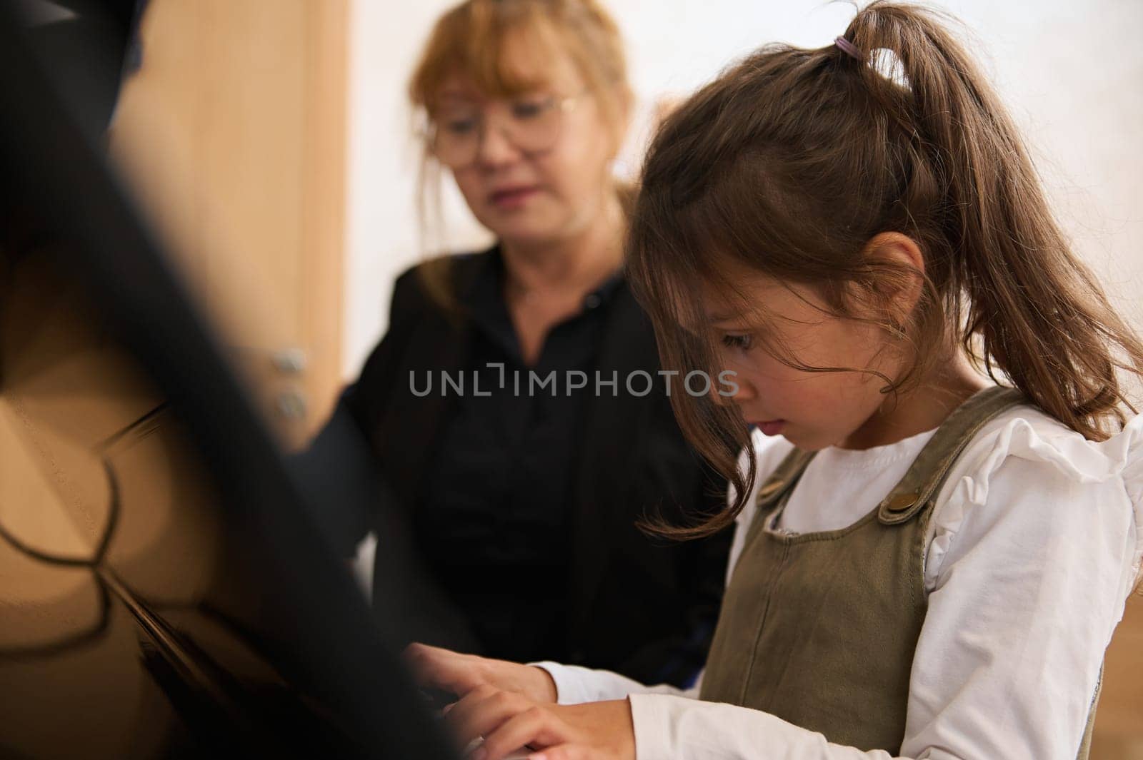 Caucasian little child girl having music class with mature female piano teacher by artgf