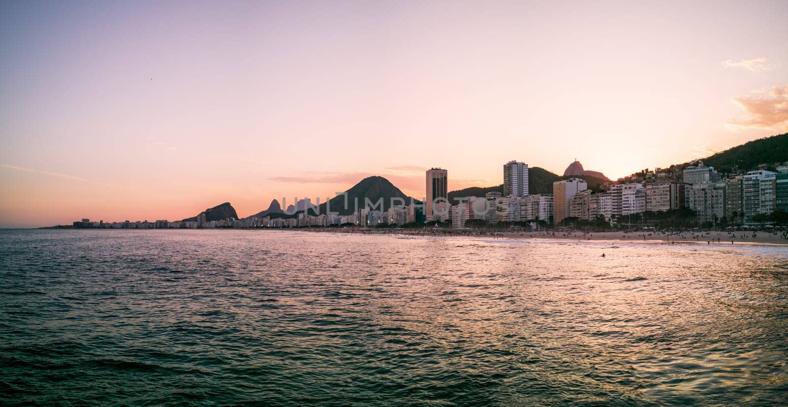 Copacabana beach at dusk featuring city lights and mountain outlines.