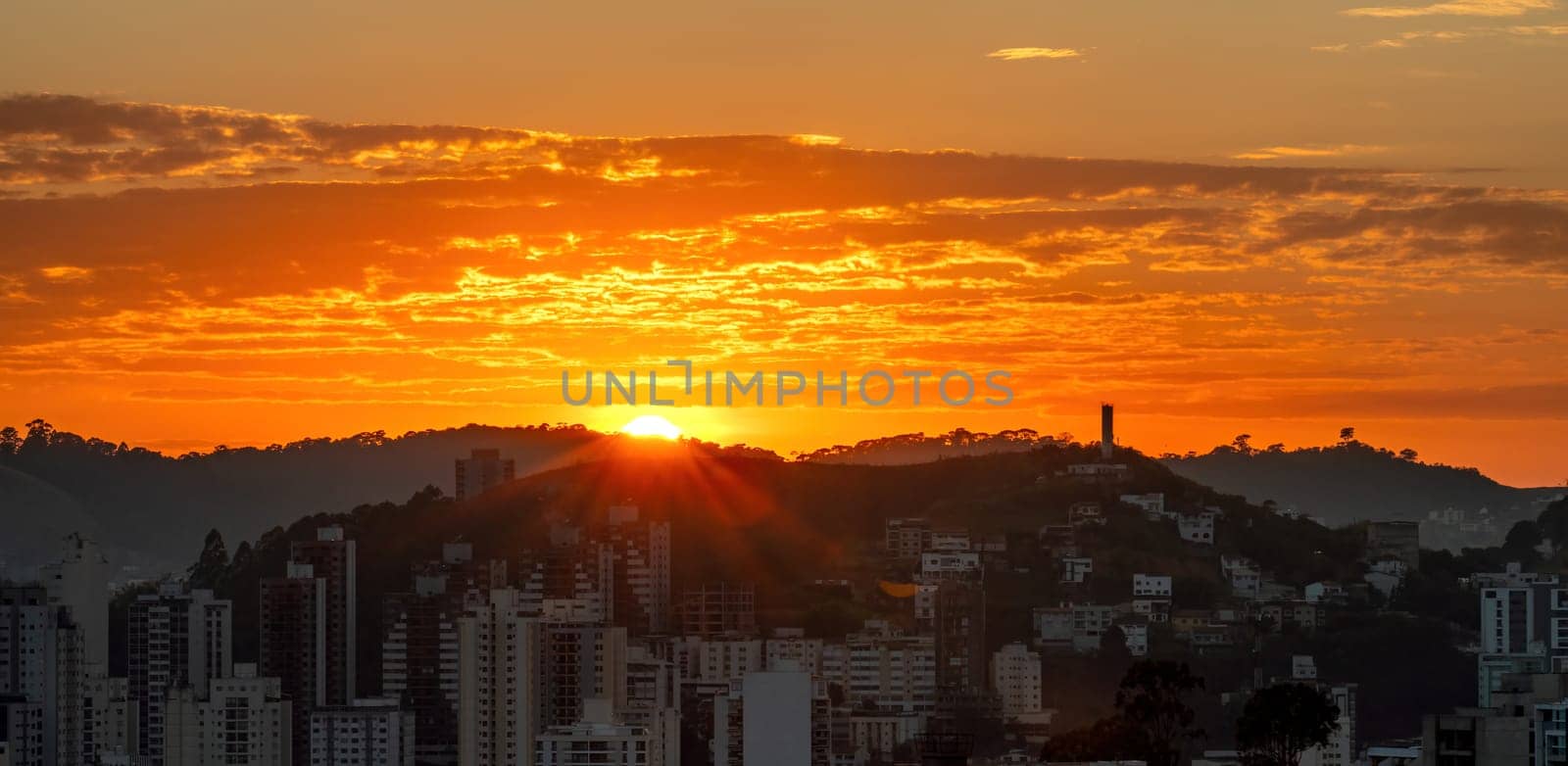 As the sun rises over the mountain at dawn, it creates an orange sky above the city, which waits in darkness for the morning light.