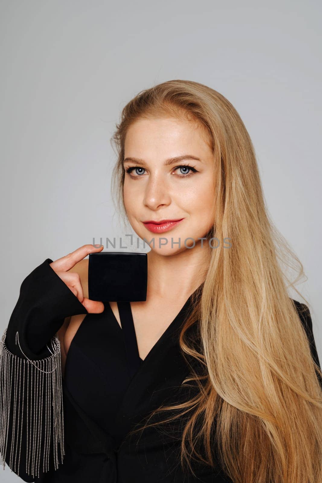 Beautiful middle-aged woman makeup artist holds shadows in her hands and looks at the camera smiling. Blond hair and a black jacket on a light background. by Matiunina