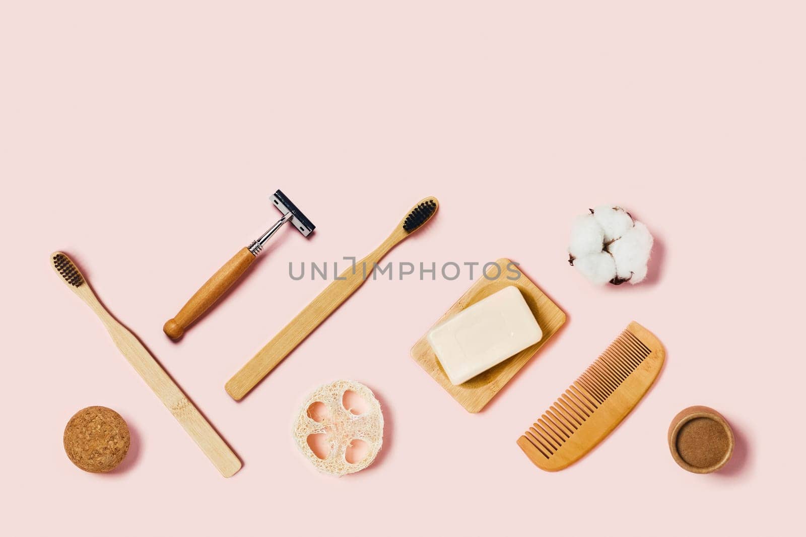 Bathroom accessories on pink background. Natural bamboo toothbrush, sponges, cotton flowers, shaving brush. Flat lay, top view.