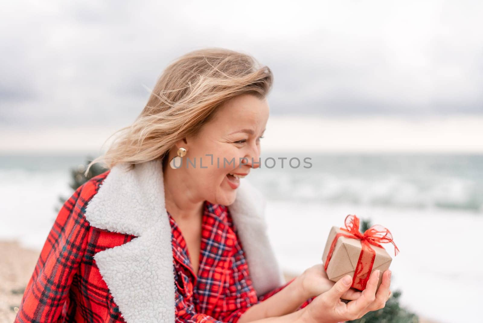 Lady in plaid shirt holding a gift in his hands enjoys beach with Christmas tree. Coastal area. Christmas, New Year holidays concep.