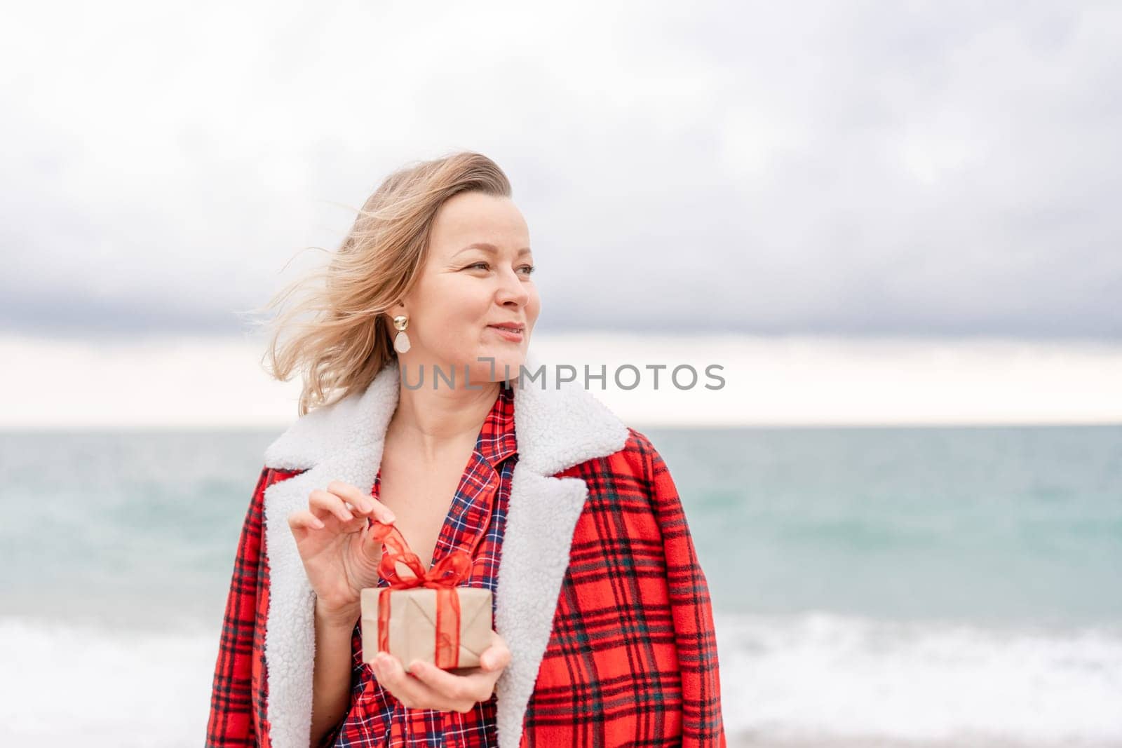 Lady in plaid shirt holding a gift in his hands enjoys beach. Coastal area. Christmas, New Year holidays concep by Matiunina