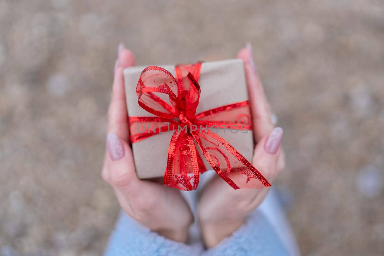 Hand holding wrapped gift with red bow. Sea Beach backdrop. The hand holding the gift is the main focus of the image, emphasizing the act of giving and receiving