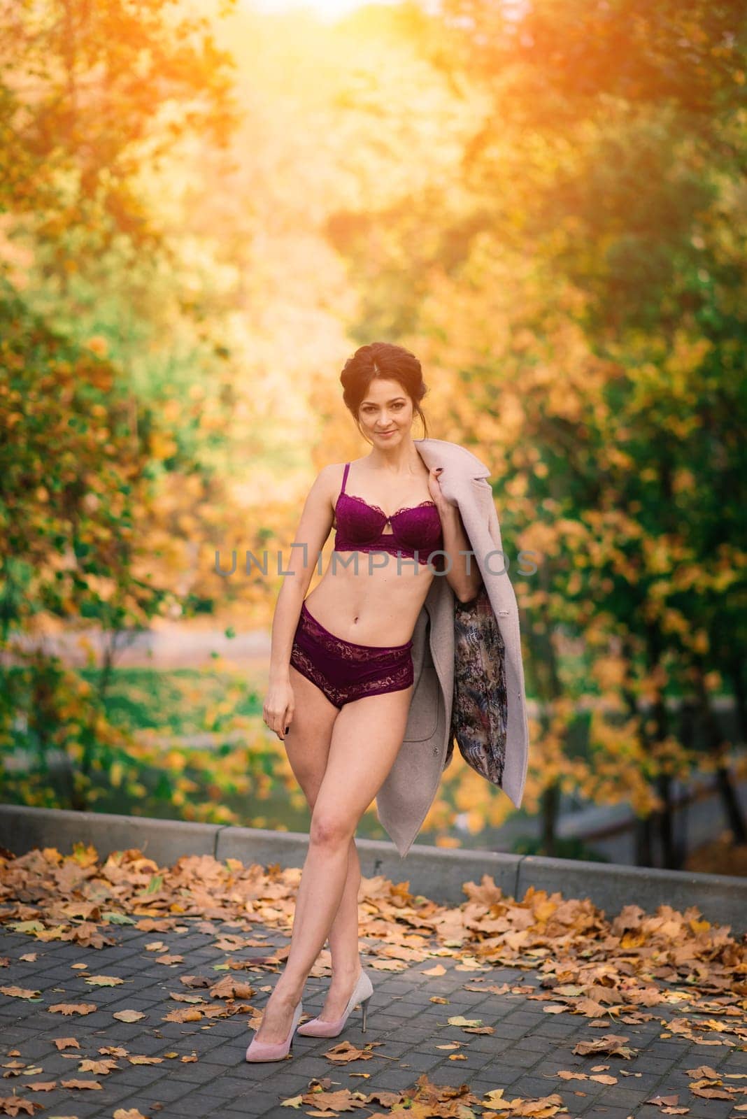 Young beautiful dark-haired woman with a slender figure posing in lingerie and a classic coat in an autumn park