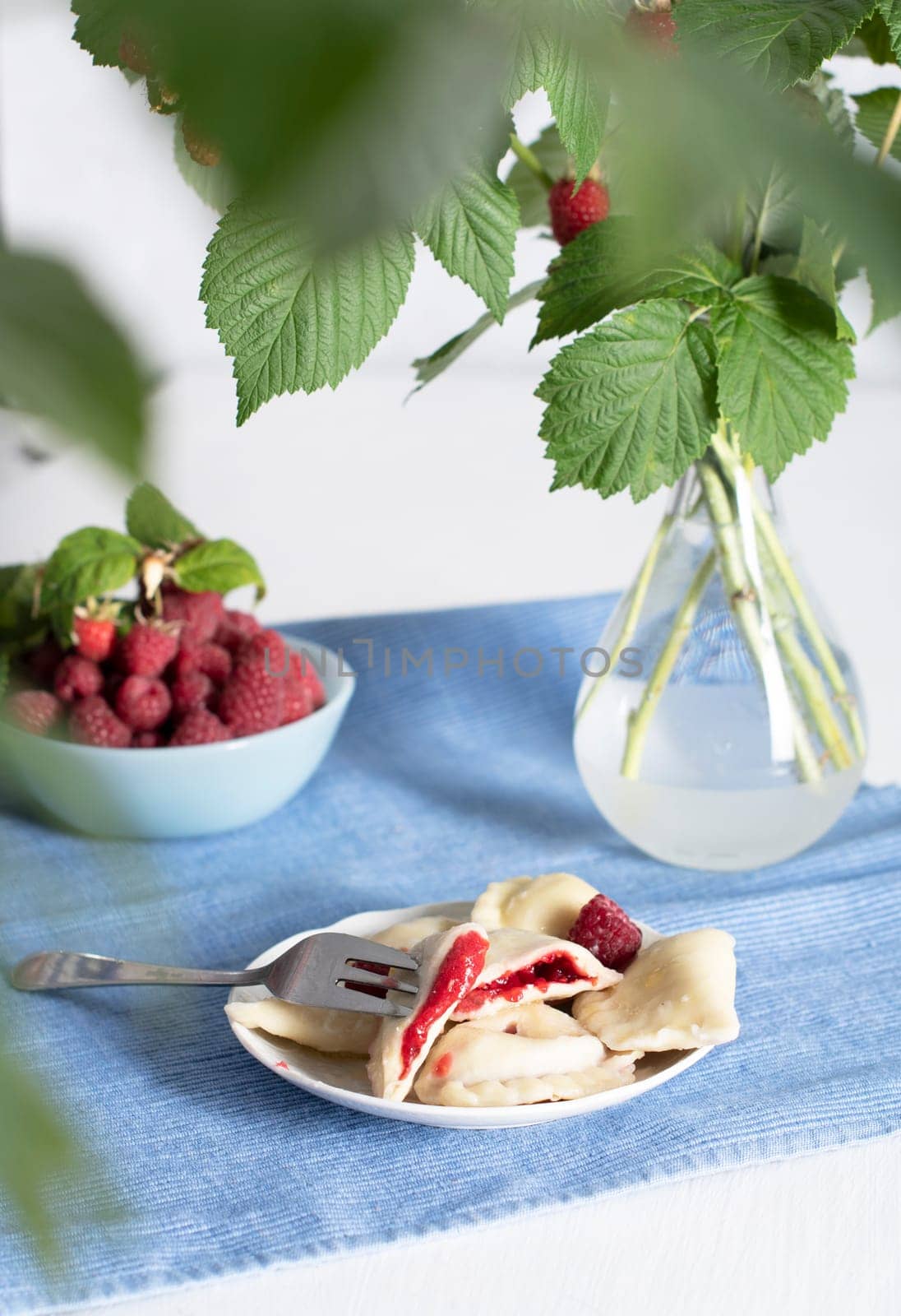 Slavic dish vareniki with fresh raspberries, Still life on a blue background with a bouquet of fresh raspberries on a branch. High quality photo