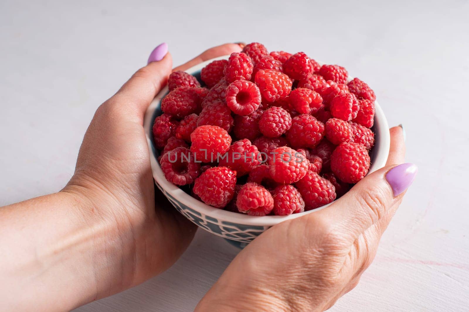 fresh raspberries in a bowl in woman hands, summer harvest fresh berries by KaterinaDalemans