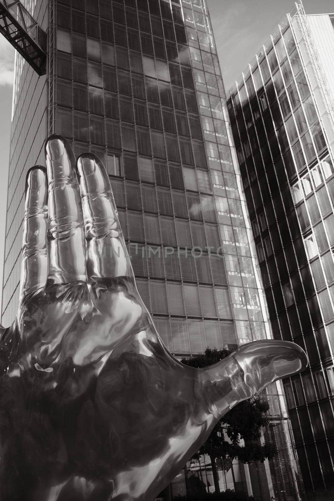 Grayscale of an Acrylic glass hand in front of the LVM glass skyscraper towers in Muenster, Germany by rherrmannde