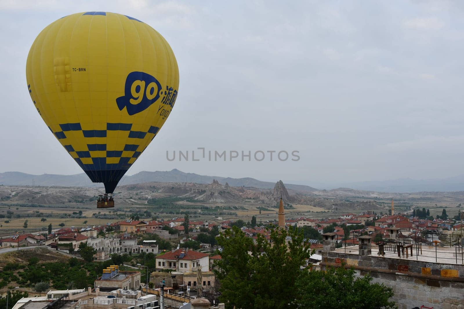 Yellow hot air balloon with the inscription go over the village of Cavusin in Cappadocia, Turkey by rherrmannde