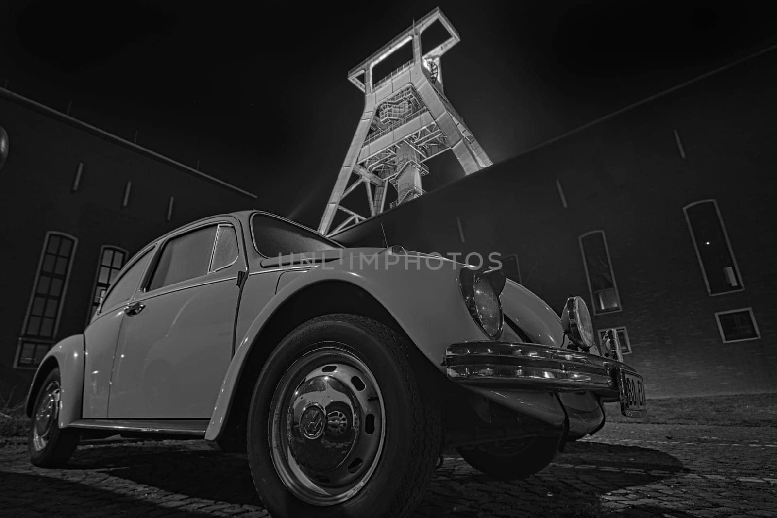 Low-angle grayscale of an old VW beetle in front of an old mining conveyor in Bochum, Germany