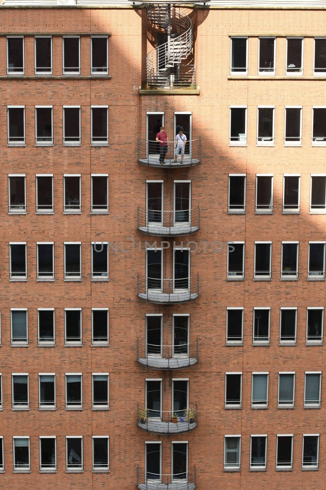 Vertical view of two men standing on the balcony of a brick-built building in Hamburg, Germany