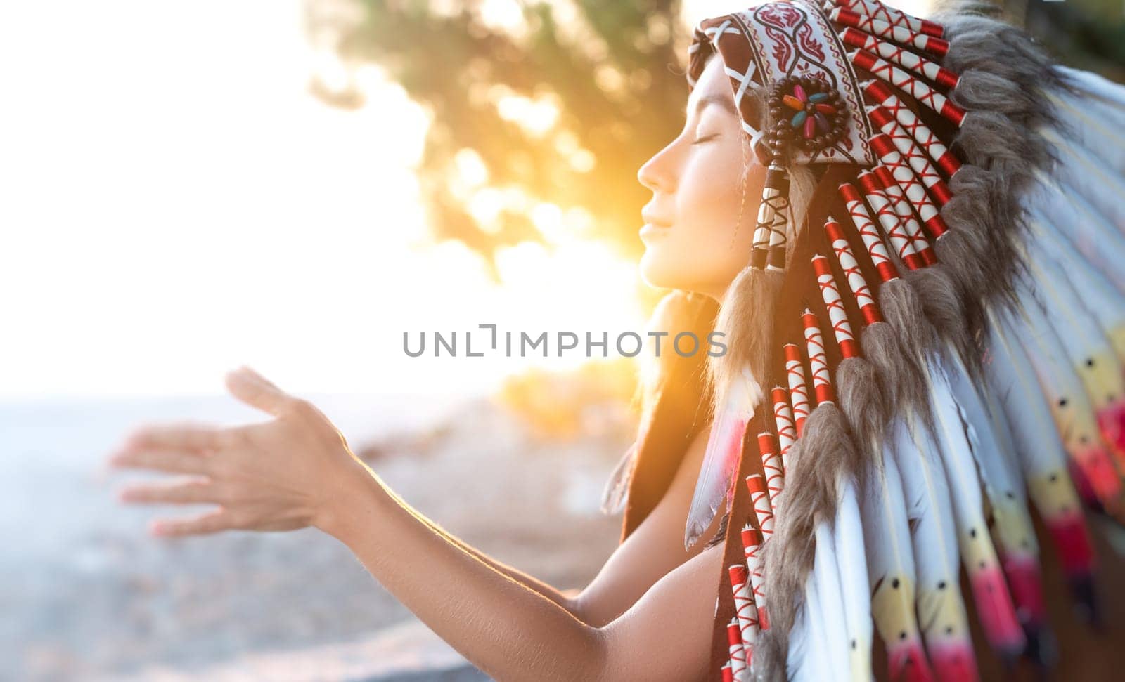 Portrait of girl with hands in Native American headdresses in nature in the sunset light by Rotozey