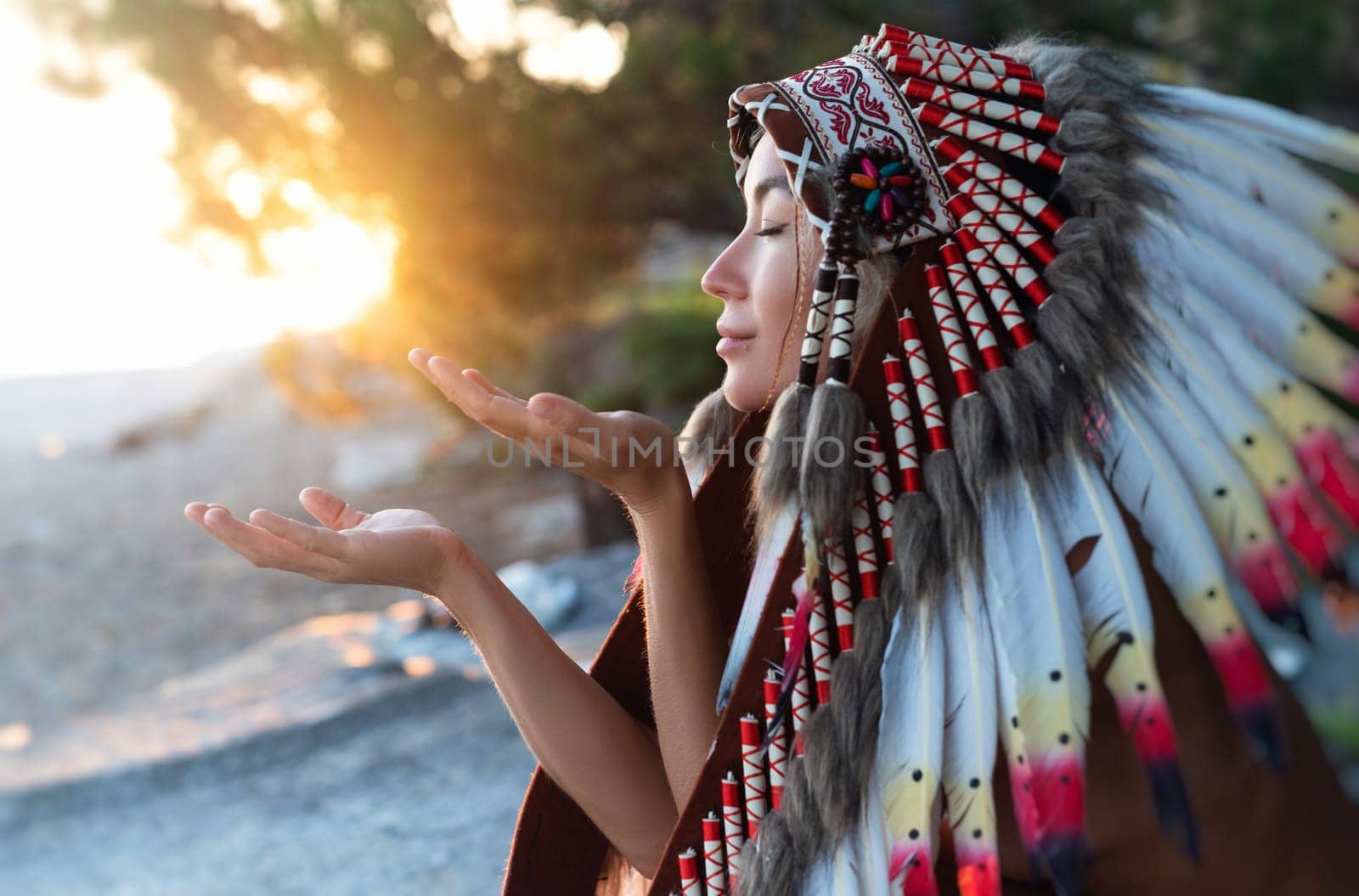 Portrait of a girl with hands in Native American headdresses in nature in the sunset light