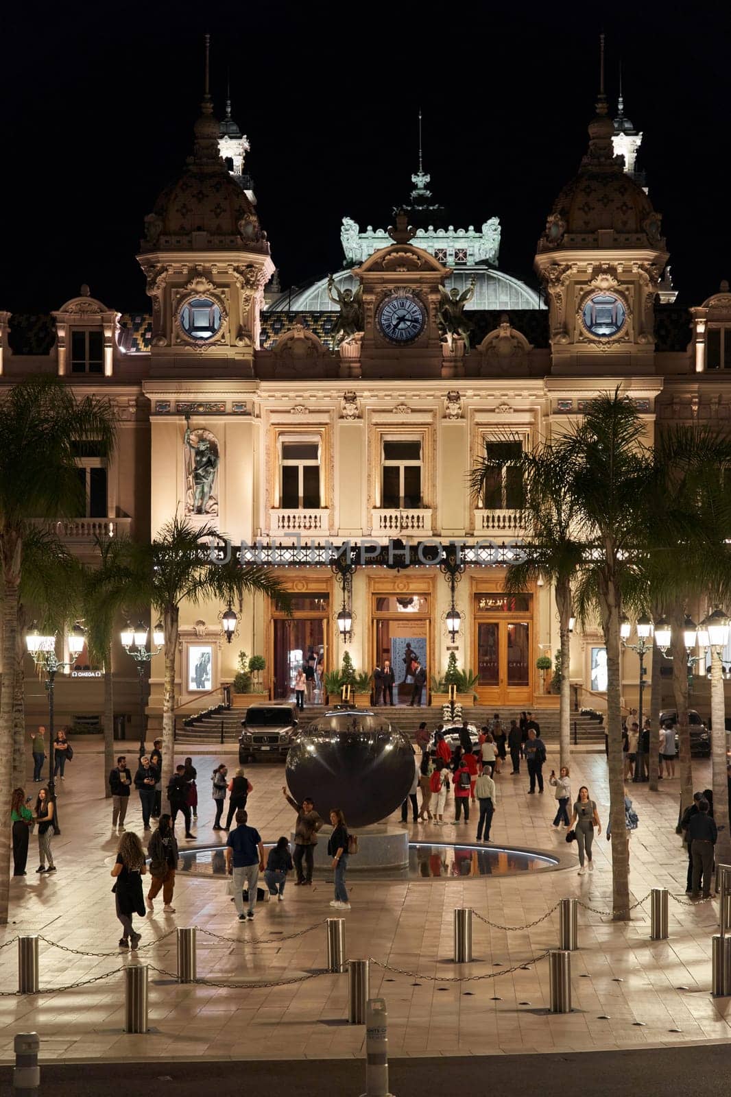 Monaco, Monte-Carlo, 12 November 2022: The famous square of Casino Monte-Carlo is at dusk, attraction night illumination, luxury cars, players, tourists, splashes of fountain. High quality photo