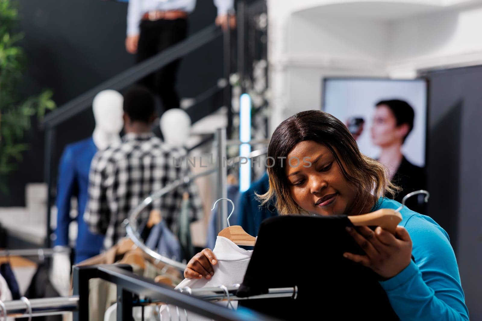 African american customer checking shirt fabric, shopping for elegant present for husband in modern boutique. Stylish woman looking at racks full with fashionable merchandise. Fashion concept