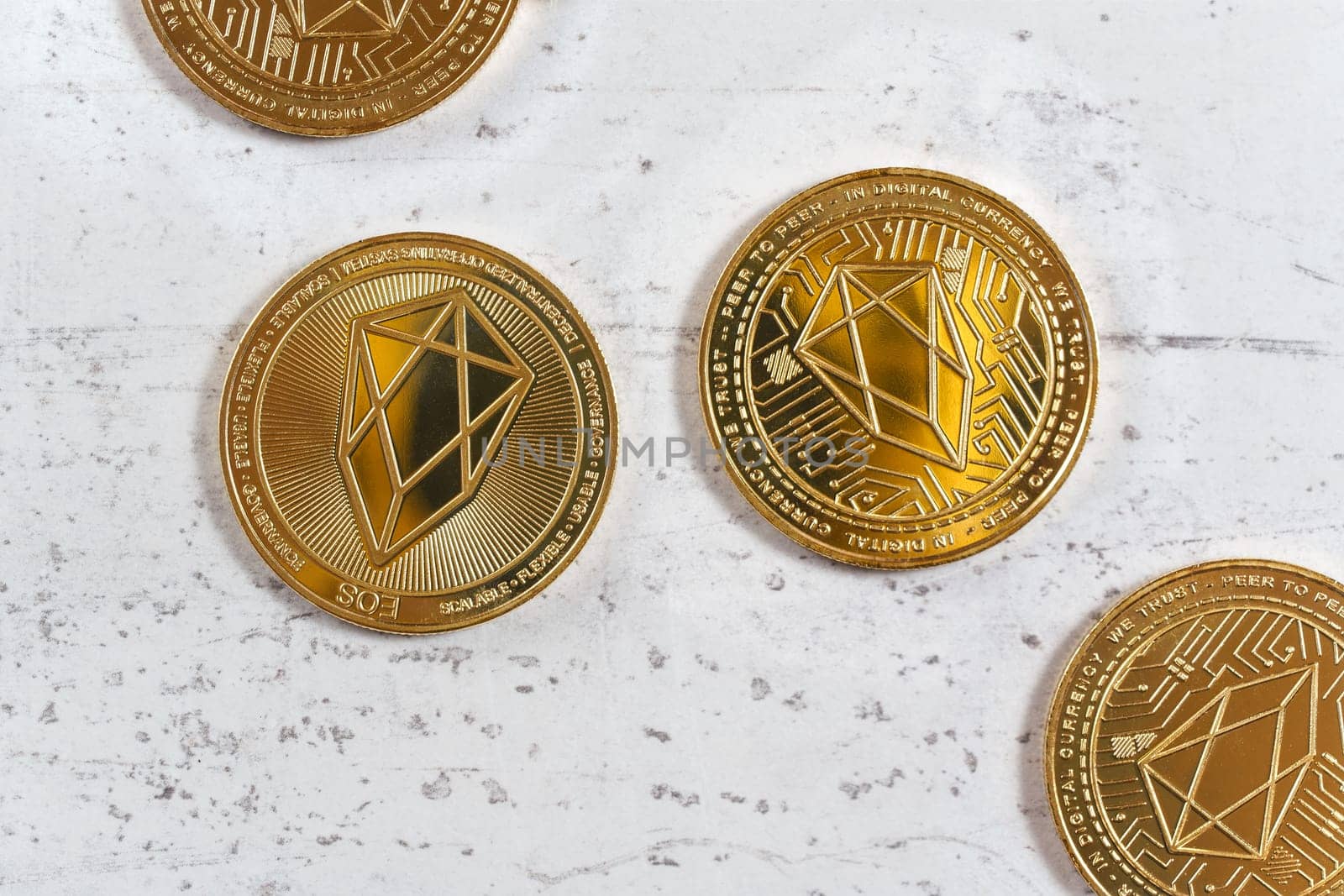 Overhead shot, golden commemorative EOS - EOSIO  cryptocurrency - coins on white stone board