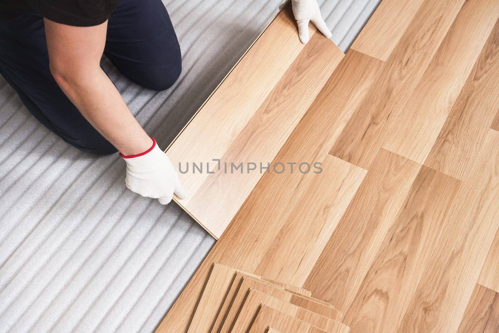 Installing laminated floor, detail on man hands holding wooden tile, over white foam base layer