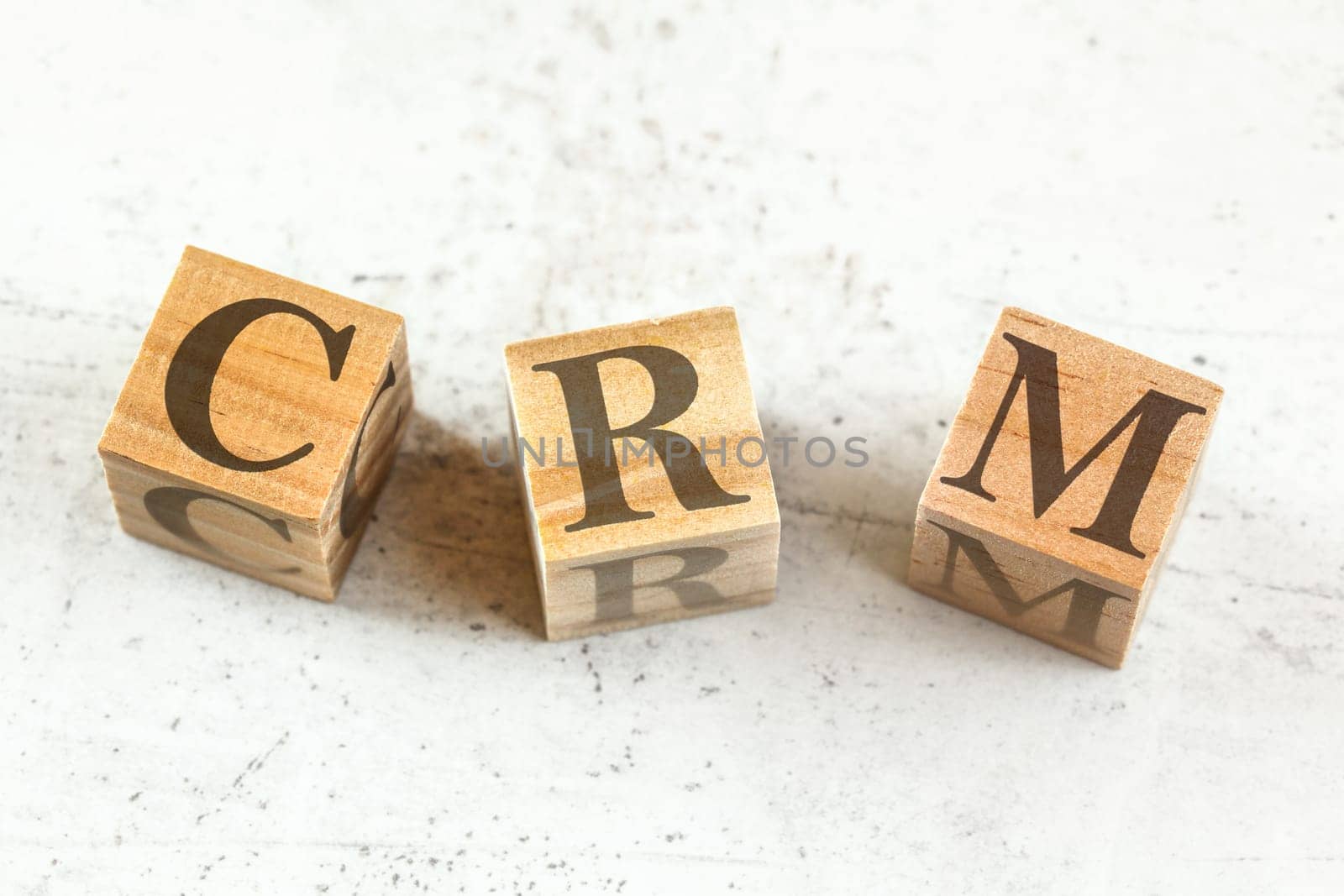 Three wooden cubes with letters CRM - stands for Customer relationship management - on white board. by Ivanko