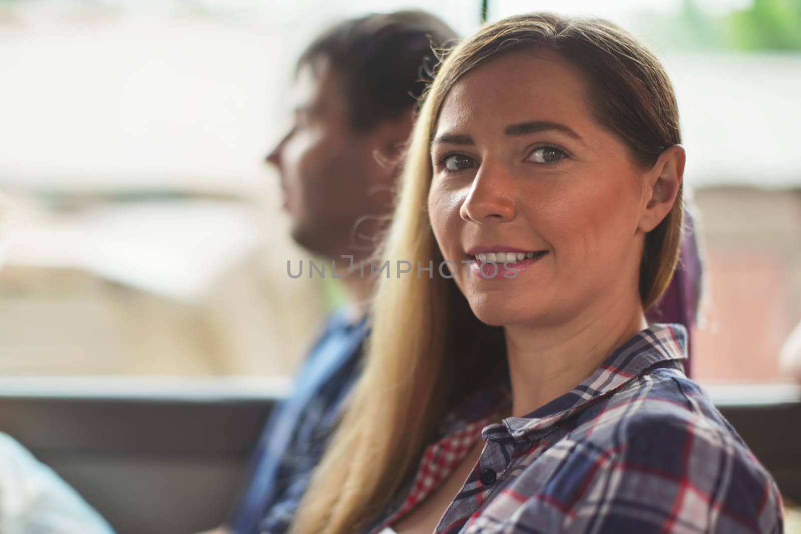 Candid portrait - young woman in shirt sitting in the bus, smiling, blurred man behind her, detail on her face