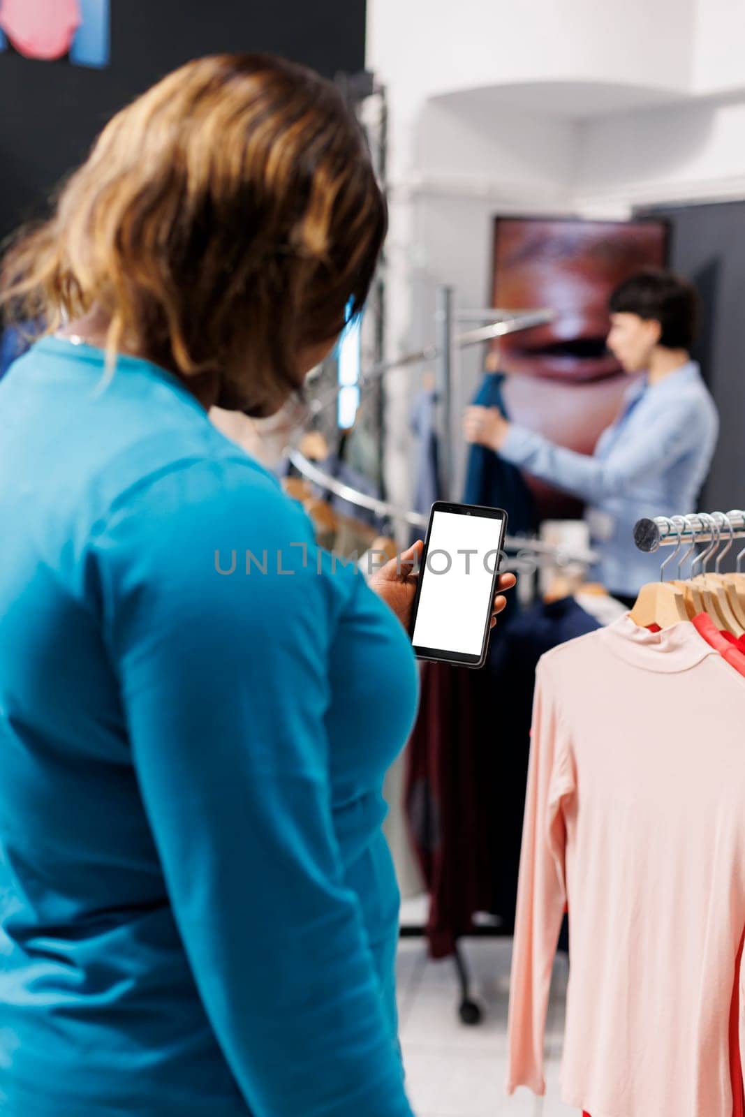 African american customer holding smartphone with white screen in shopping mall, checking fashion store app. Stylish woman buying fashionable merchandise in modern boutique. Technology concept