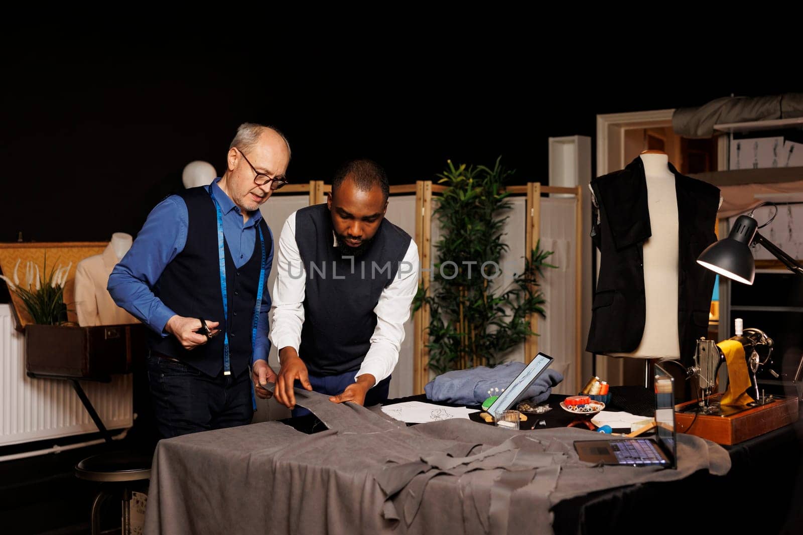 Professional craftsman and apprentice cutting textile material with scissors in atelier studio, designing upcoming fashion collection. Tailors manufacturing bespoke attire, working with fabric