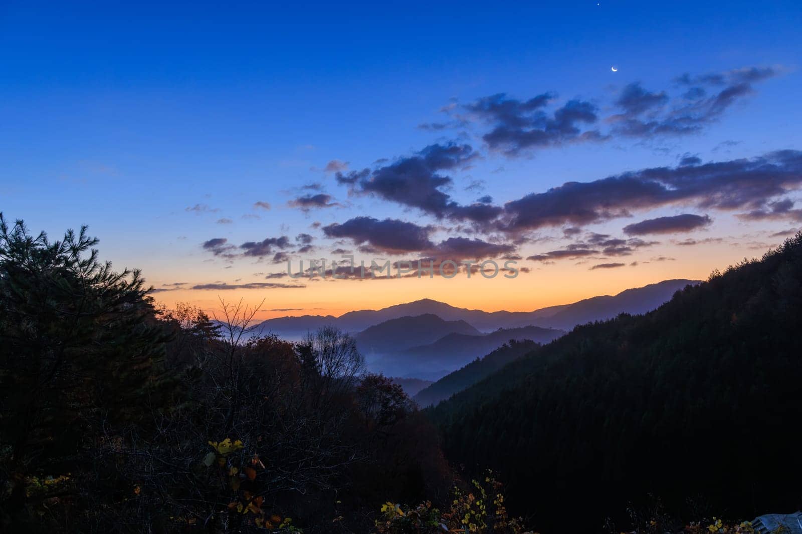 Dawn fog and mist in mountain valley with sunrise glow and moon in sky. High quality photo