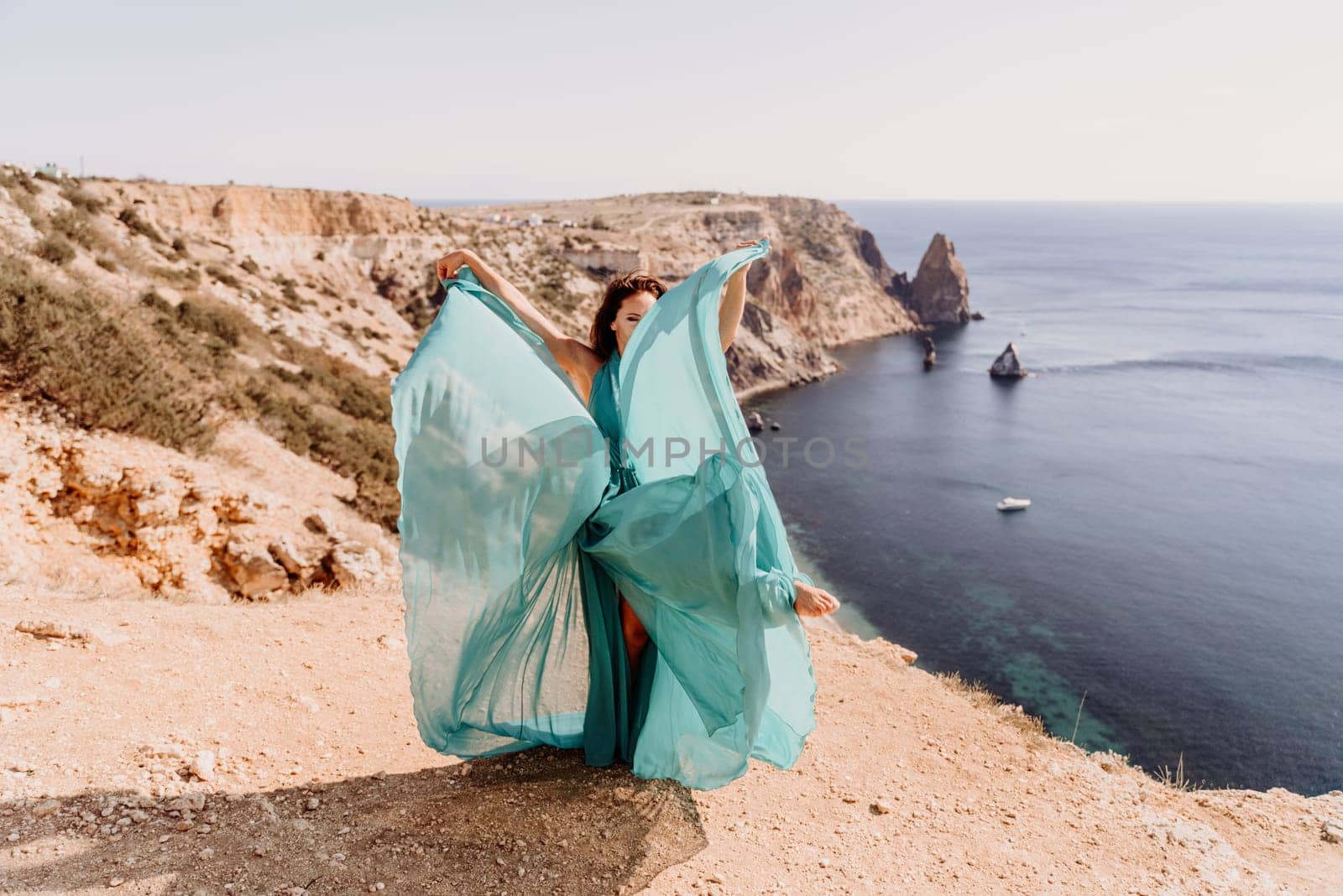 Woman green dress sea. Female dancer posing on a rocky outcrop high above the sea. Girl on the nature on blue sky background. Fashion photo