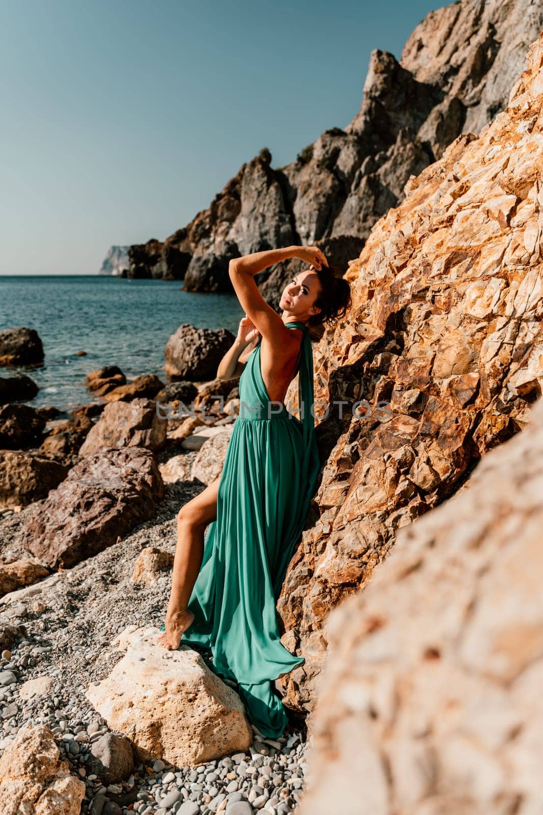 Woman green dress sea. Woman in a long mint dress posing on a beach with rocks on sunny day. Girl on the nature on blue sky background