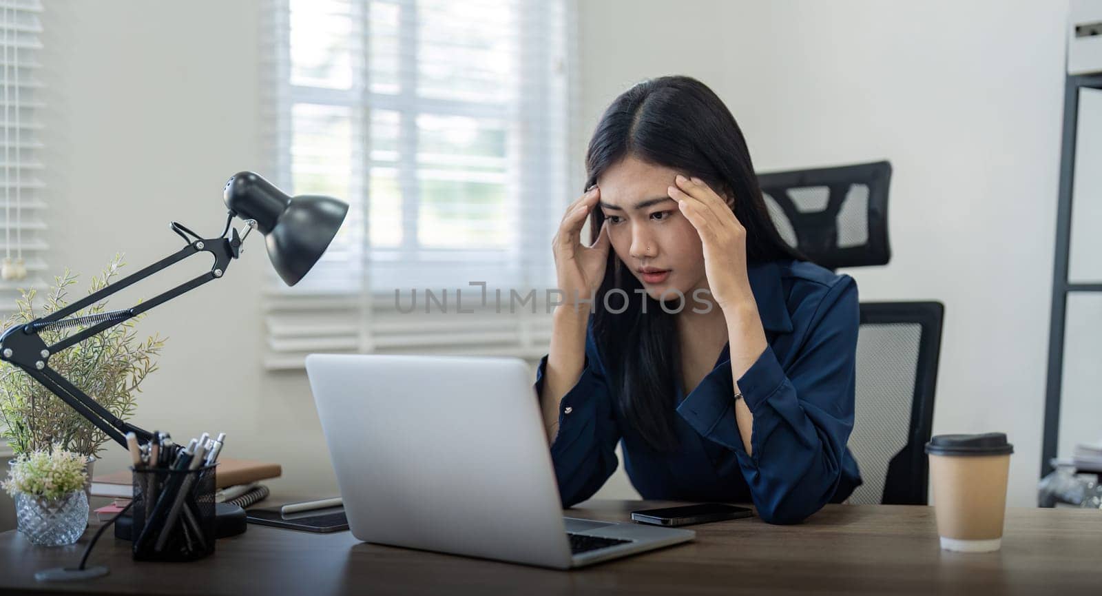 Stressed business woman looking worried, tired and overwhelmed while working with laptop on a desk in the office at home by nateemee