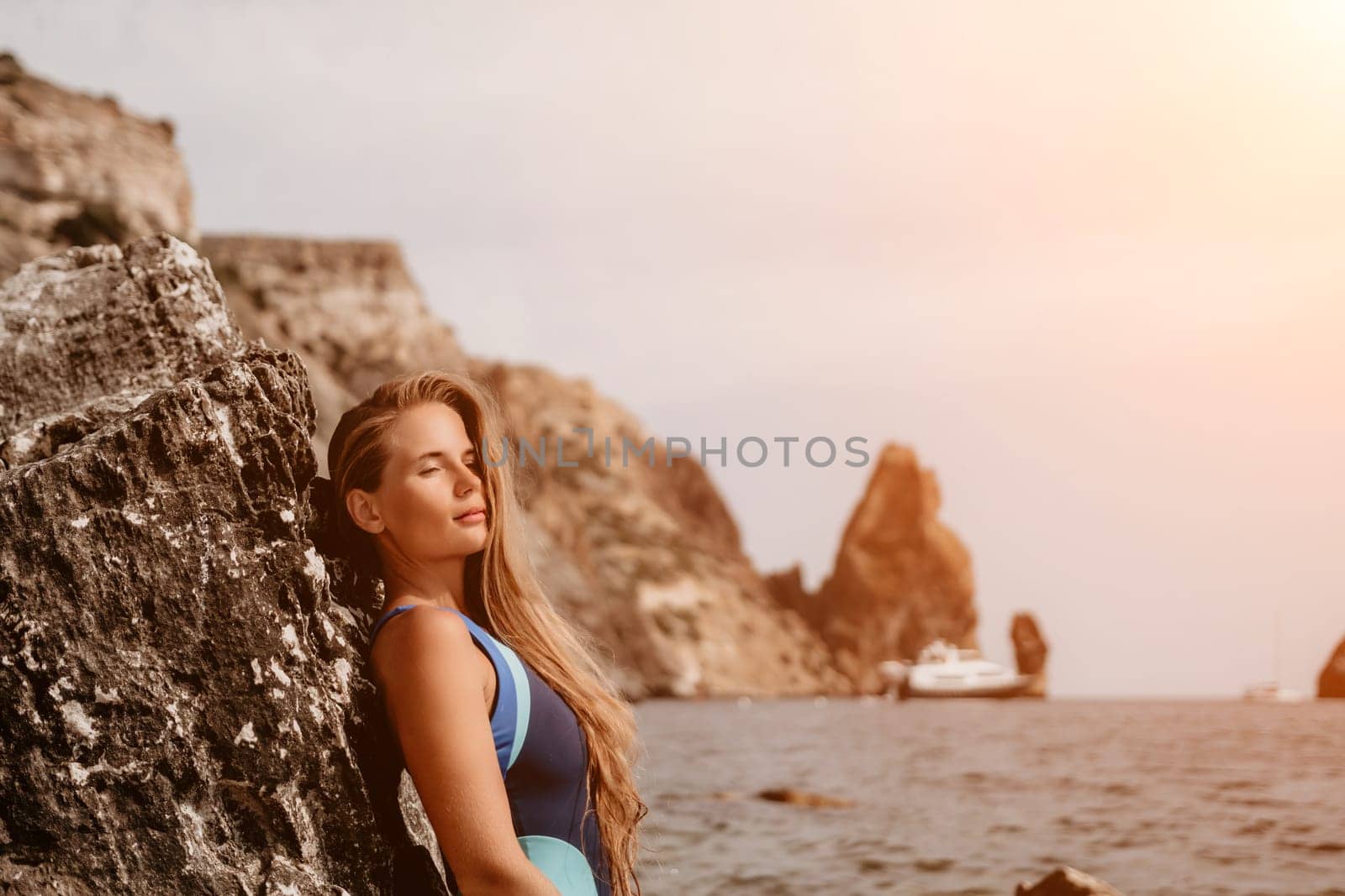 happy tourist in blue swimwear takes a photo outdoors to capture memories. The photo depicts a woman traveling and enjoying her surroundings on the beach, with volcanic mountains in the background