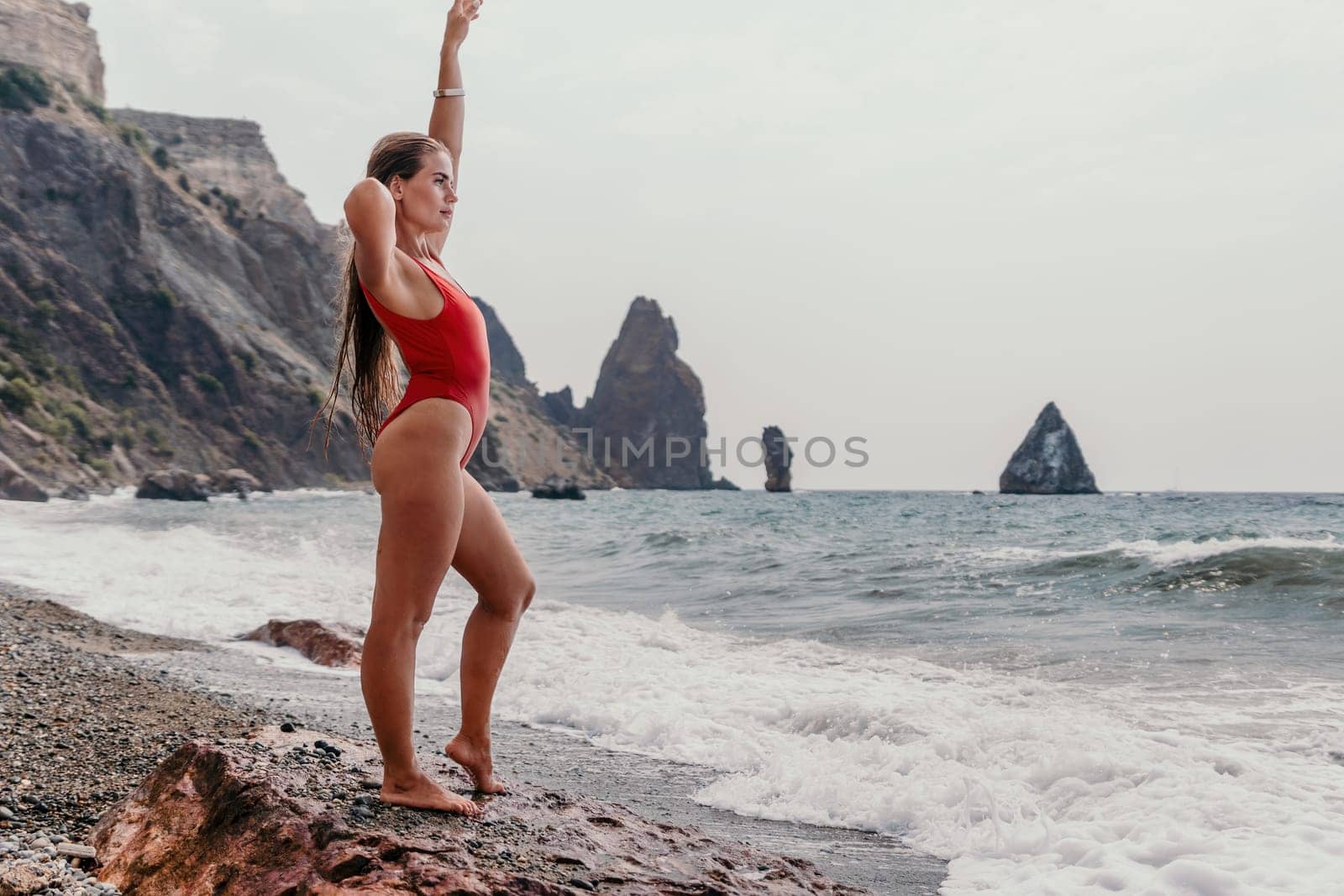 Woman summer travel sea. Happy tourist in red bikini enjoy taking picture outdoors for memories. Woman traveler posing on beach at sea surrounded by volcanic mountains, sharing travel adventure joy by panophotograph