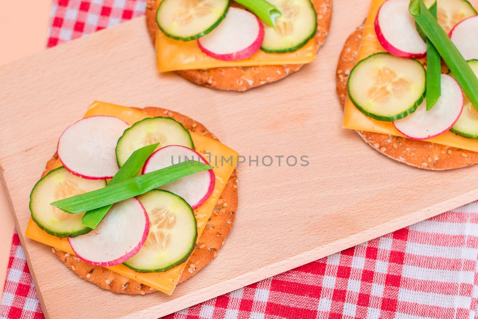 Light Breakfast. Quick and Healthy Sandwich. Fresh Cucumber and Radish with Green Onions and Cheese on Crispy Cracker on Wooden Cutting Board
