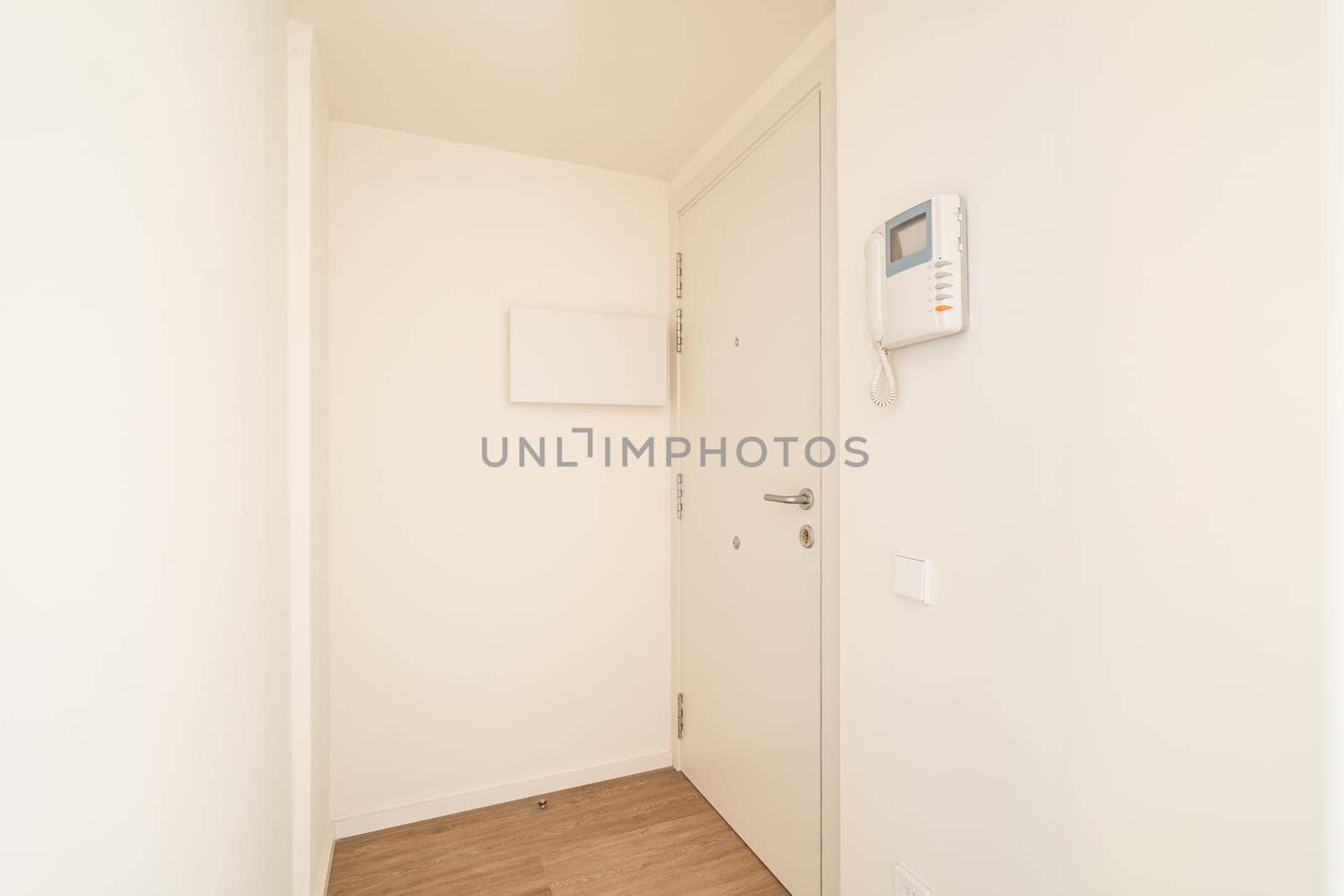Big safe entrance door in hallway with light-colored walls. Corridor with front door and intercom system on wall after apartment renovation