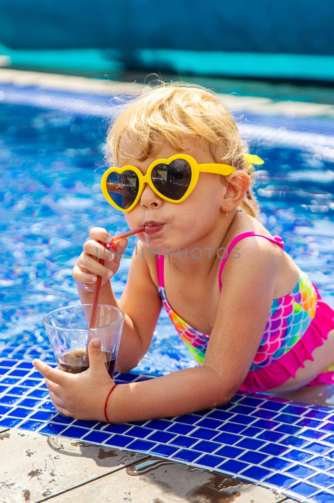 A child near the pool in sunglasses drinks a cocktail. Selective focus. Kid.