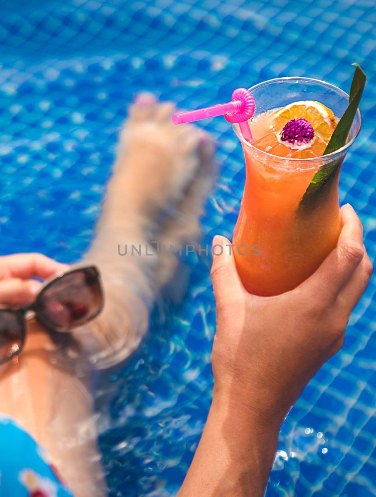 A woman in the pool drinks a cocktail. Selective focus. Kid.