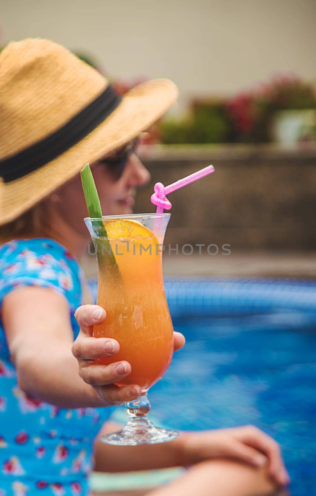 A woman in the pool drinks a cocktail. Selective focus. Kid.