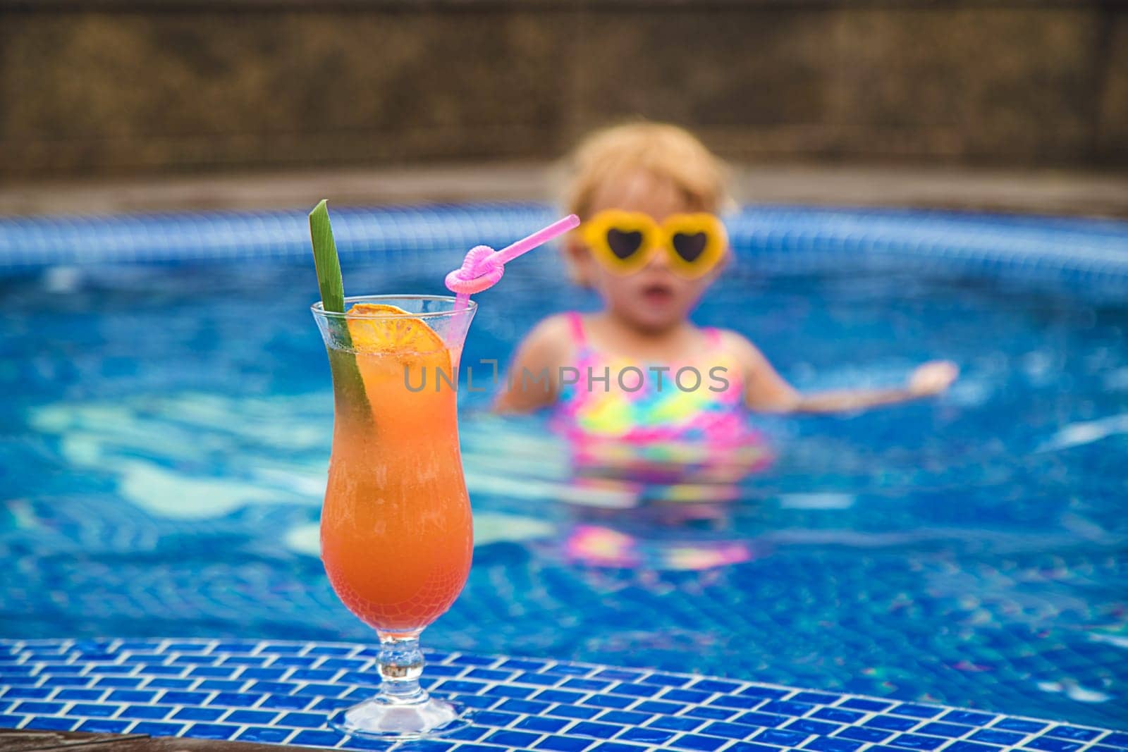 A child in the pool drinks a cocktail. Selective focus. Kid.