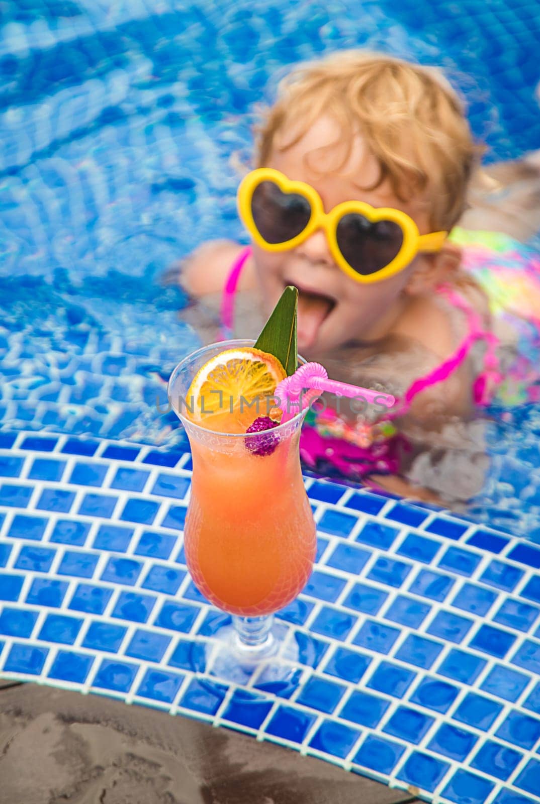 A child in the pool drinks a cocktail. Selective focus. Kid.